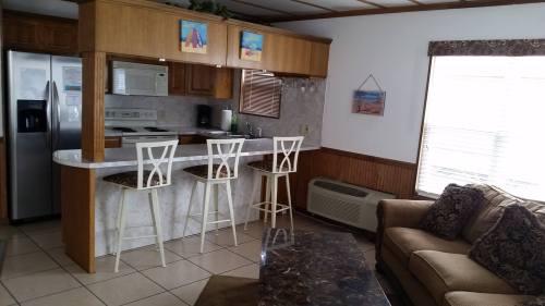 A cozy kitchen with a bar area, three white stools, and a living room featuring a sofa and coffee table.