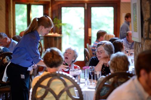 A waitress serves a table of diners in a cozy restaurant, with guests engaged in conversation and enjoying their meals.