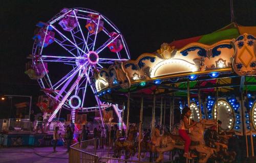A brightly lit carnival scene at night featuring a Ferris wheel and a carousel with colorful lights.