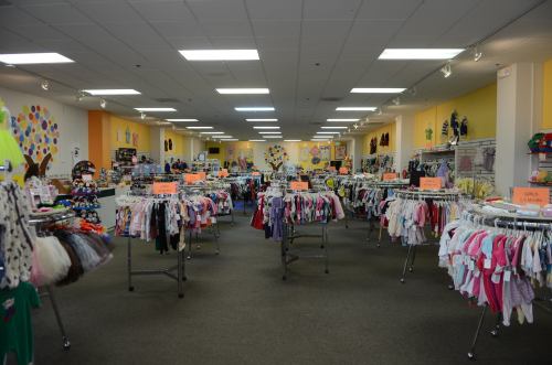 A brightly lit retail store with racks of children's clothing and colorful displays along the walls.