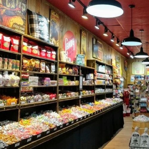 A colorful candy store display with various sweets and snacks arranged on shelves against a wooden wall.