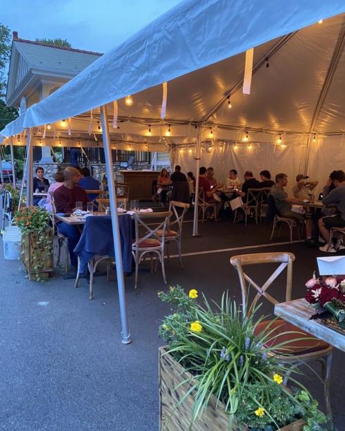 Outdoor dining setup under a tent, with string lights and tables filled with diners enjoying their meals.