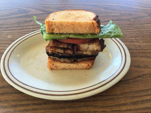 A grilled sandwich with lettuce, tomato, and layers of cooked meat on toasted bread, served on a plate.