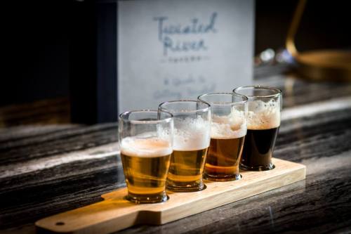 A wooden flight board holds four small glasses of different beers on a marble countertop.