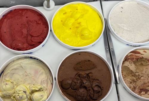 A variety of ice cream tubs in different flavors, including red, yellow, brown, and cream, arranged in a display.