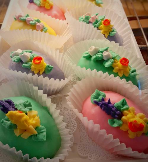 Colorful, decorative Easter egg-shaped confections with floral icing, arranged in paper liners.