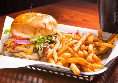 A juicy cheeseburger with lettuce, tomato, and bacon, served with a side of crispy French fries on a tray.
