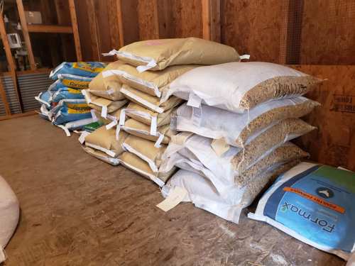 A stack of bags filled with various grains and materials, arranged neatly in a wooden storage space.