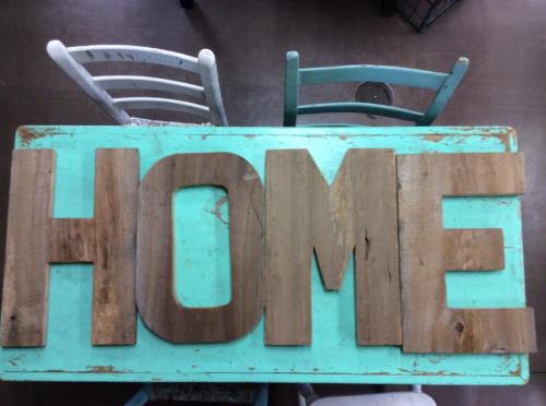 Wooden letters spelling "HOME" arranged on a rustic, turquoise table with chairs in the background.