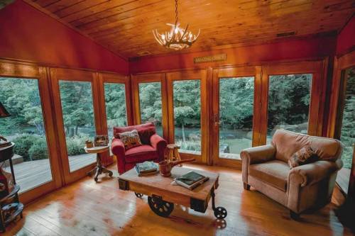 Cozy sunroom with wooden walls, two chairs, a coffee table, and large windows overlooking a lush green landscape.