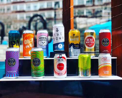 A display of various colorful beer cans arranged on a shelf, with a sunny outdoor background.