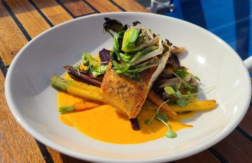 A beautifully plated dish featuring seared fish atop vibrant vegetables and a creamy orange sauce.