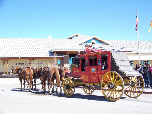 A colorful horse-drawn stagecoach parked in front of a building, with people gathered nearby.