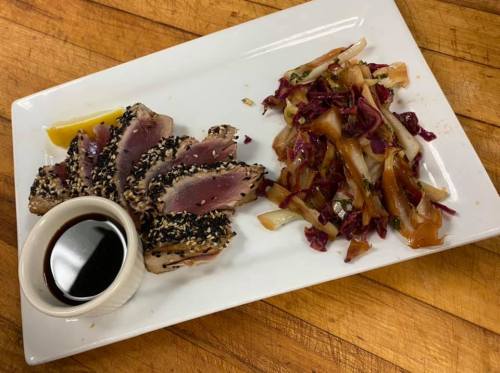 A plate featuring sliced sesame-crusted tuna, a lemon wedge, and a side of sautéed vegetables.