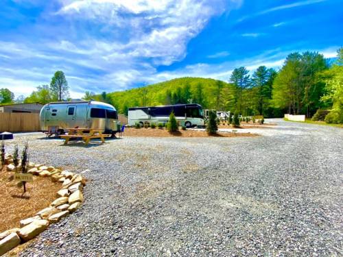 A gravel campsite with Airstream trailers and motorhomes surrounded by trees and blue skies.