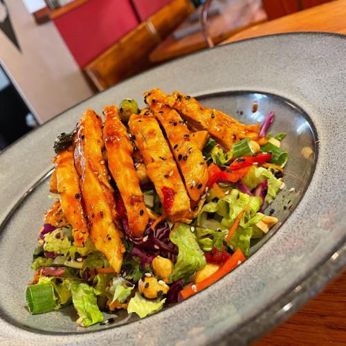 A colorful salad topped with grilled chicken strips, sesame seeds, and mixed greens on a gray plate.