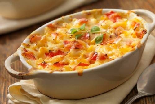 A creamy pasta bake with red peppers and cheese, served in a white dish on a wooden table.