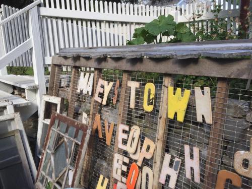 A collection of colorful, vintage letters arranged on a wooden frame, with a white picket fence and greenery in the background.