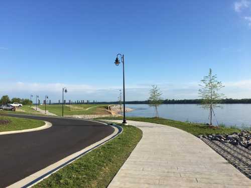 A scenic pathway along a river, lined with lamp posts and greenery under a clear blue sky.