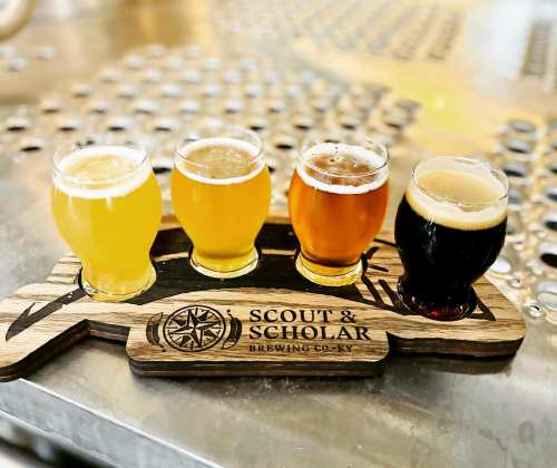 A wooden flight board holds four glasses of different craft beers at Scout & Scholar Brewing Co.