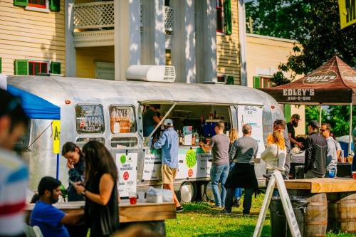 A food truck serves customers at an outdoor event, with people enjoying food and drinks in a lively atmosphere.
