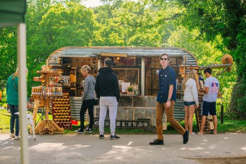 A vintage food truck with people gathered around, enjoying food and drinks in a green outdoor setting.