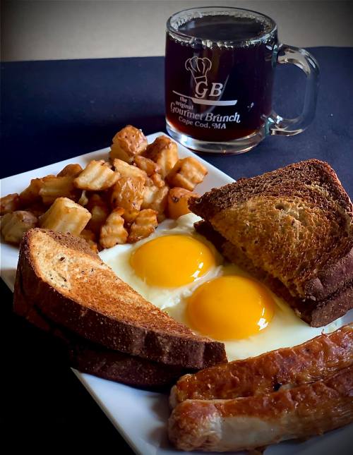 A plate with two sunny-side-up eggs, toast, sausage, and crispy potatoes, alongside a mug of coffee.