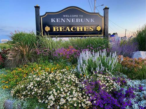 Sign welcoming visitors to Kennebunk Beaches, surrounded by colorful flowers and greenery.