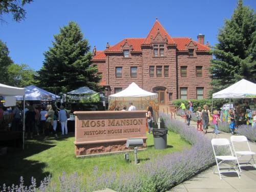 A historic mansion with a red roof, surrounded by tents and people at an outdoor event, with lavender in the foreground.