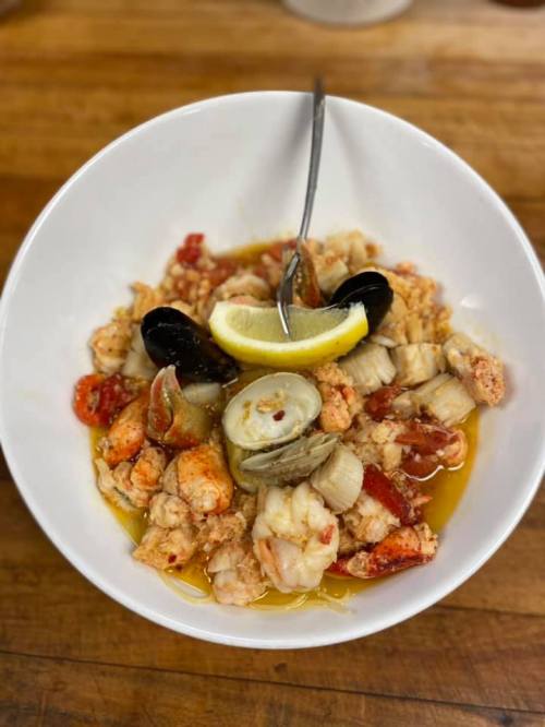A bowl of seafood featuring shrimp, clams, and mussels, garnished with lemon and served in a flavorful broth.