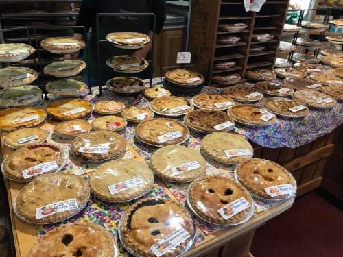 A display of various pies on a table, each labeled, showcasing a colorful assortment of flavors and crusts.