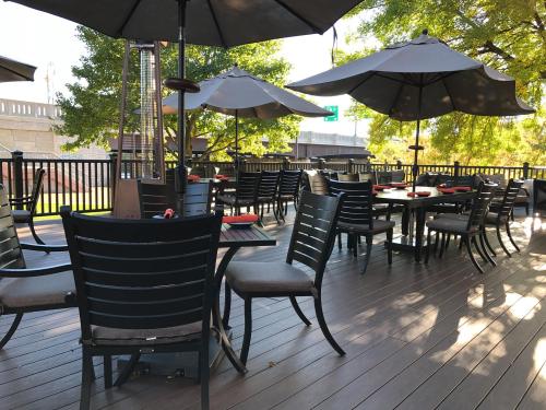 Outdoor dining area with black chairs and tables, shaded by large umbrellas, surrounded by trees and a wooden deck.
