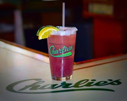 A colorful cocktail with a lime wedge and straw sits on a bar with the name "Charlie's" in the background.