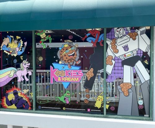 Colorful window mural featuring cartoon characters, cookies, and playful designs for "Kookies & Kream" shop.