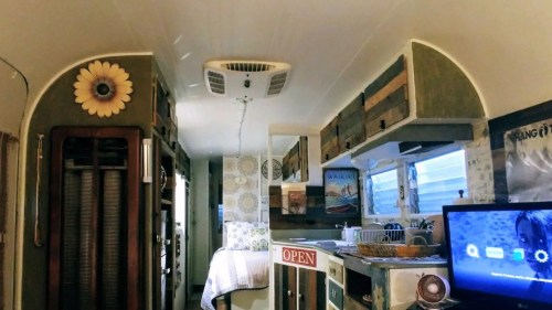 Interior of a cozy, vintage-style camper with wooden accents, a small kitchen area, and a TV.