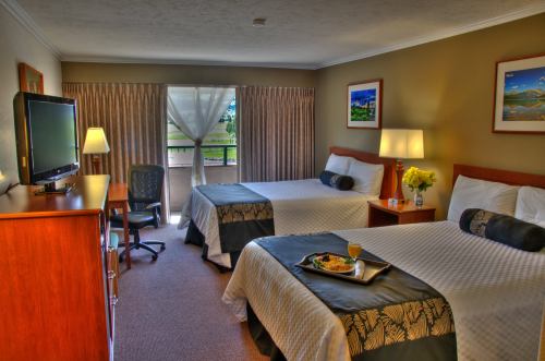 A cozy hotel room with two beds, a TV, a desk, and a balcony view, featuring warm lighting and decorative artwork.