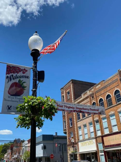 A street lamp with a banner for the West Virginia Strawberry Festival and an American flag against a blue sky.