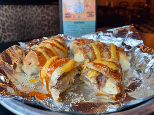 A platter of stuffed rolls drizzled with cheese and sauce, served on foil in a cozy restaurant setting.