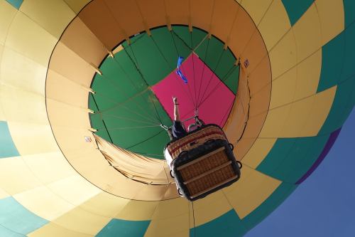 A colorful hot air balloon viewed from below, with a person in the basket reaching upward.