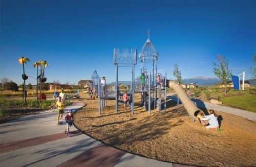 Children play on a modern playground with slides and climbing structures under a clear blue sky.