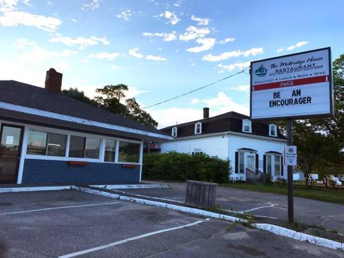 A restaurant with a sign reading "BE AN ENCOURAGER" and a blue exterior, surrounded by greenery and a clear sky.