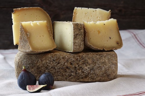 A selection of various cheeses stacked on a stone, accompanied by fresh figs on a linen cloth.