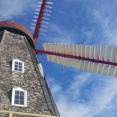 A close-up of a windmill's wooden structure and blades against a blue sky with scattered clouds.