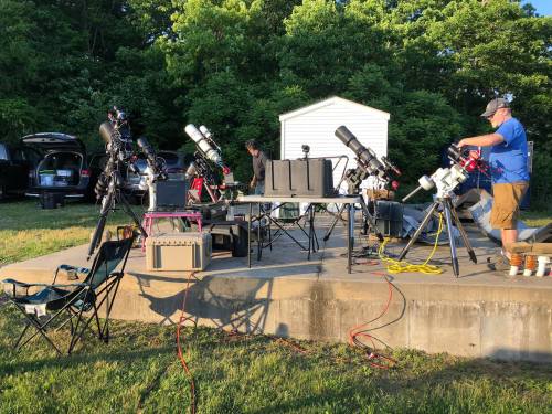 A setup of telescopes and equipment on a patio, with people preparing for stargazing in a green outdoor setting.