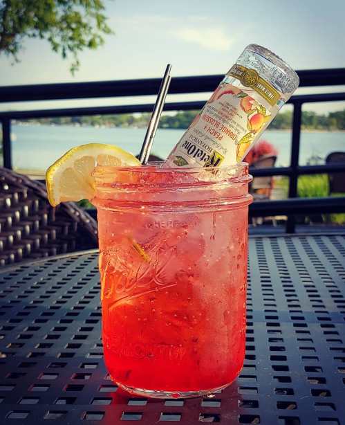 A refreshing pink cocktail in a mason jar, garnished with a lemon slice and a bottle of flavored drink.