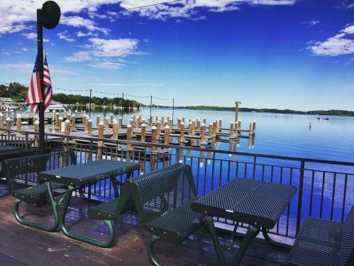 A peaceful lakeside view with picnic tables, a flag, and a dock under a clear blue sky.