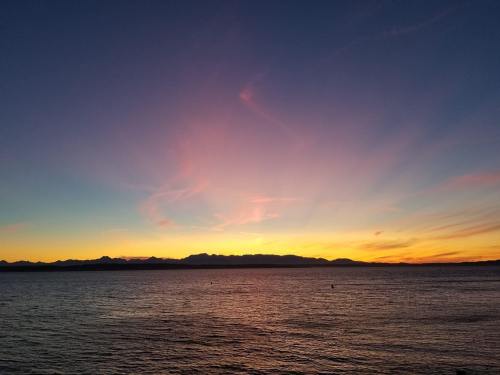 A serene sunset over a calm ocean, with colorful clouds and distant mountains silhouetted against the sky.