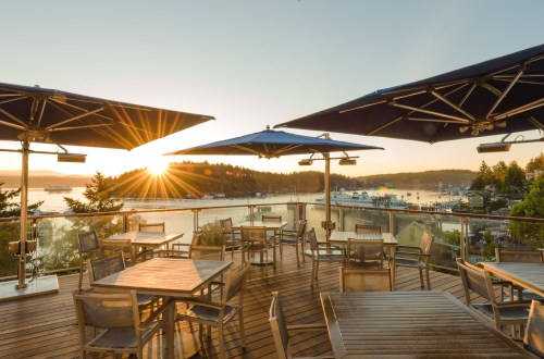 Sunset view from a deck with tables and umbrellas overlooking a marina and boats in the water.