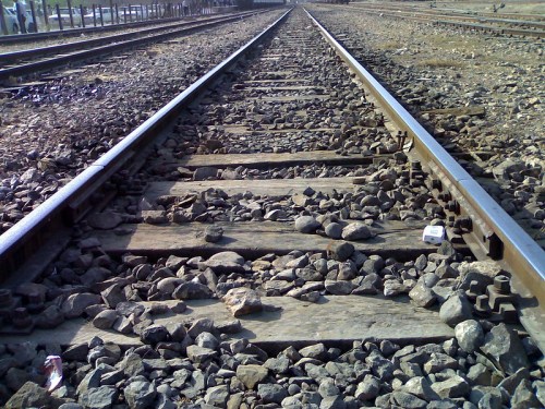 Close-up view of railway tracks with wooden ties and gravel, stretching into the distance.
