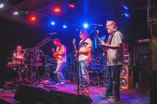 A band performs on stage with instruments and colorful lights in a lively music venue.